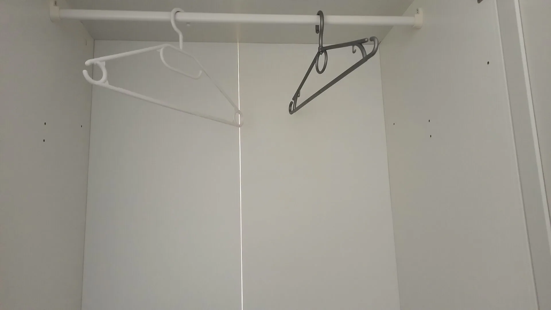 真實衣櫃吊掛衣物與背側光線縫隙照片，示意要巡檢背板、衣物密度與空氣交換路徑